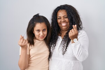 Mother and young daughter standing over white background doing money gesture with hands, asking for salary payment, millionaire business