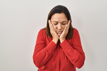 Hispanic mature woman standing over white background with sad expression covering face with hands while crying. depression concept.