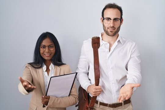 Interracial business couple wearing glasses smiling cheerful offering palm hand giving assistance and acceptance.