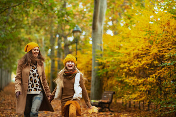 happy mom and child walking outdoors in city park in autumn