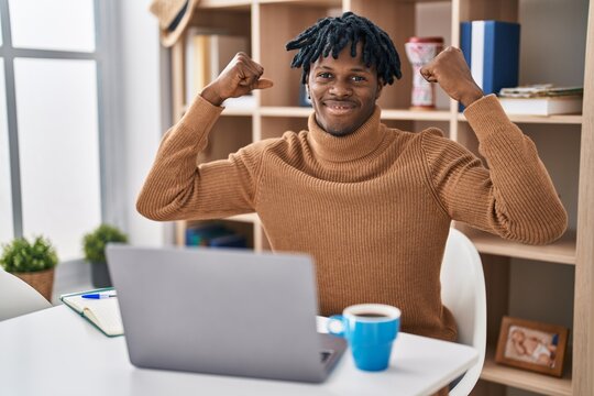 Young african man with dreadlocks working using computer laptop showing arms muscles smiling proud. fitness concept. - Powered by Adobe