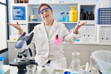 Hispanic girl with down syndrome working at scientist laboratory smiling cheerful offering hands giving assistance and acceptance.