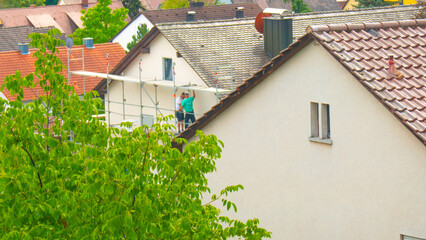 Construction and repair of the house. Builders on scaffolding on city background.The cost of...