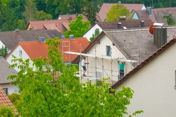 Home construction. Roof repair and tile replacement. Builders on scaffolding on city background.The cost of building a house in Europe.Construction and repair of the house.