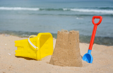 Beautiful sand castle, child plastic shovel and bucket on beach near sea