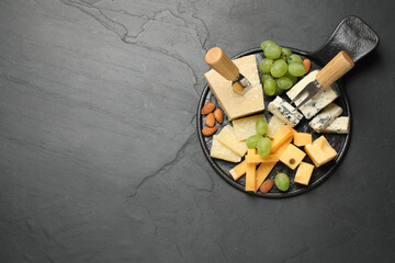 Cheese platter with specialized knife and fork on black table, top view. Space for text