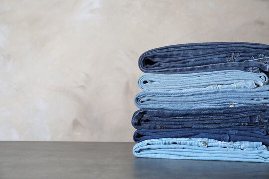 Stack of different jeans on grey table. Space for text