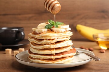 Pouring honey onto pancakes with sliced banana on wooden table
