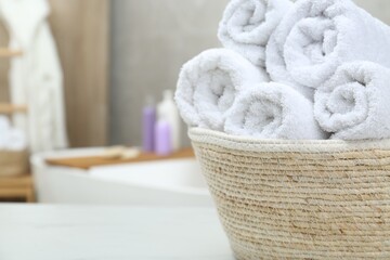 Obraz na płótnie Canvas Wicker basket with rolled bath towels on white table in bathroom, closeup. Space for text