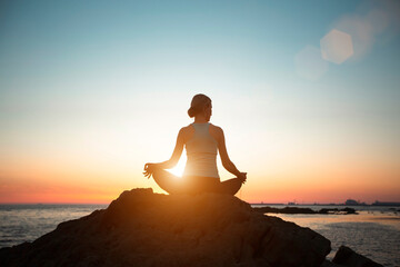 Silhouette of a woman doing yoga in the lotus position on the beach during a beautiful sunset.