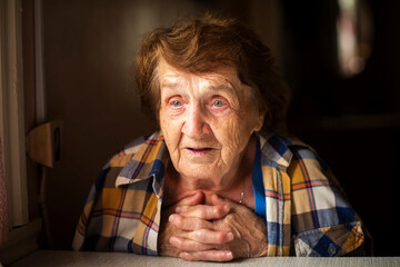 A portrait of an elderly woman in someone else's shirt slung over her shoulders, in her own home.