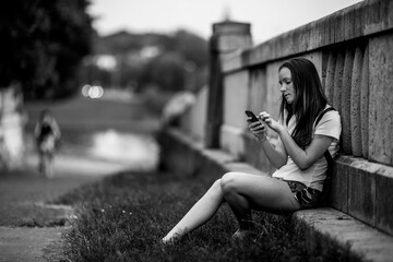 A girl taiping text on her cell phone outdoors. Black and white photo.