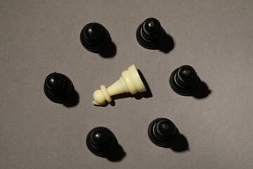 Black chess pieces and white one on grey background, flat lay. Bullying concept