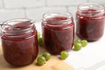 Jars of delicious gooseberry jam and fresh berries on white table, closeup