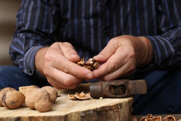 Man cracking walnuts with hammer at table, closeup - Powered by Adobe