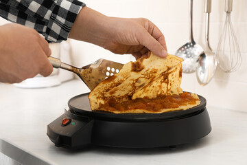 Man cooking delicious crepe with jam on electric pancake maker in kitchen, closeup