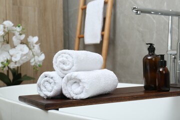 Rolled towels and personal care products on tub tray in bathroom