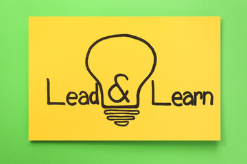 Sheet of paper with light bulb drawing and words Lead, Learn on green background, top view