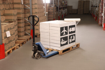 Manual pallet truck with stacked boxes with shipping icons and roll of stretch wrap in warehouse