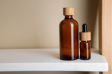 Glass bottles of cosmetic products on white shelf, space for text