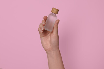 Woman holding bottle of cosmetic product on pink background, closeup