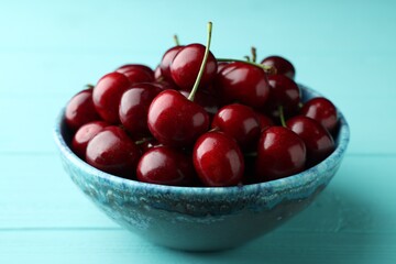 Fresh ripe cherries in bowl on turquoise wooden table, closeup