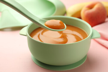 Spoon with tasty pureed baby food over bowl on pink wooden table, closeup