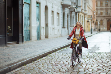 Fototapeta na wymiar elegant woman in red rain coat outdoors in city riding bicycle