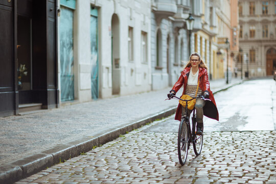 elegant woman in red rain coat outdoors in city riding bicycle