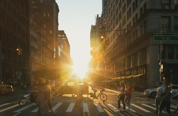 People, bikes and taxis in a busy intersection on 5th Avenue in New York City with sunset shining in the background