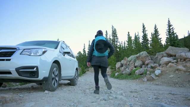 Hikers walking on a gravel road past a white SUV to the trailhead during dusk, static