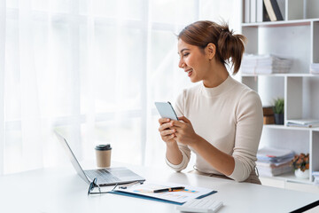 Young Pretty Asian businesswoman using smartphone when working at desk in office.