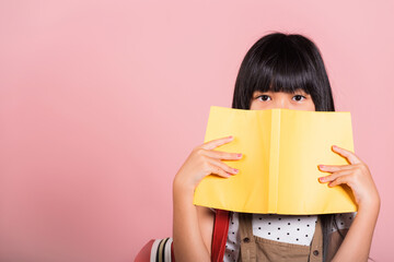 Asian little kid 10 years old holding and reading yellow book near eyes at studio shot isolated on...