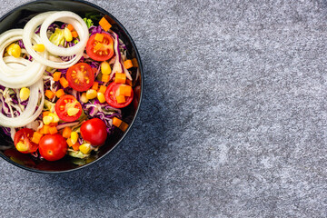Top view of the healthy colorful salad bowl with tomatoes fresh mixed leaves vegetable in a dish on cement stone table background, Health salad snack diet food weight loss concept
