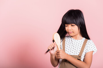 Asian little kid 10 years old hold comb brushing her unruly she touching her long black hair at...