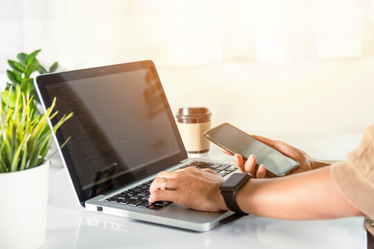 Software developer hands typing data coding programming javascript with laptop computer and mobile phone, Programmer woman looking smartphone program code at workplace, IT startup concept