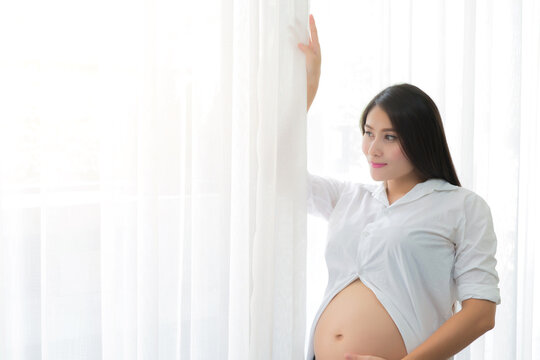 Young mother or pregnant woman standing near window in living room at home