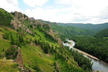 View of a picturesque valley with a river flowing along the edge of the taiga at the foot of a high mountain range.