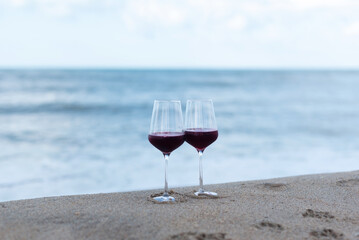 Two glasses of red wine stand on the shore of the blue sea