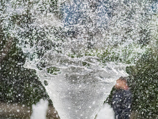 Splashes of water on dark background. Water sprays in sunny day close-up.