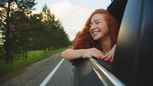 free woman travels by car catches wind with hand from car window. Girl with long hair is sitting in front seat of car, stretching her arm out window and catching glare of setting sun. Hand rays of sun