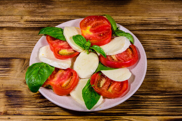 Plate with caprese salad (italian salad with cherry tomatoes, mozzarella cheese and basil leaves) on wooden table
