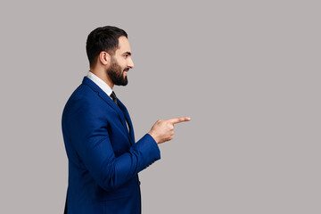 Side view of bearded man pointing finger away with toothy smile on face, empty space for your...