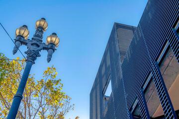 Low angle view of street light with three lamps and building with metal walls in San Francisco, CA