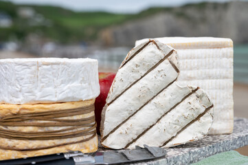 Four famous cheeses of Normandy, squared pont l'eveque, round camembert cow cheese, yellow livarot, heartshaped neufchatel and view on alebaster cliffs Porte d'Aval in Etretat, Normandy, France