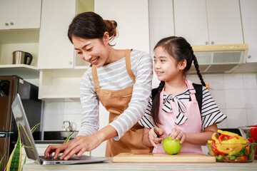 Single mother and daughter enjoy preparing salad from Video tutorial from computer notebook