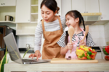 Asian mother and daughter preparing salad and using online method from computer notebook