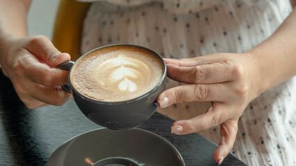 Woman's hand holding coffee cappuccino in black mug.