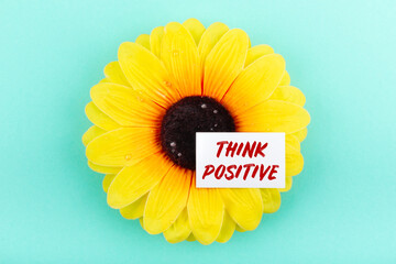 Text think positive on a white card on a large yellow flower. Мotivation concept.