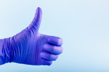Hand in blue medical glove showing ok sign. Giving thumbs up sign. Protection concept.